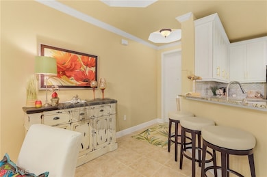 Kitchen featuring a breakfast bar area, crown molding, white cabinetry, backsplash, and light tile patterned flooring