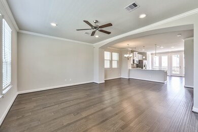 This spacious open-concept living area features hardwood floors, ample natural light from large windows, a ceiling fan, and recessed lighting. It flows seamlessly into a modern kitchen with an island, pendant lights, and access to a balcony through glass doors.