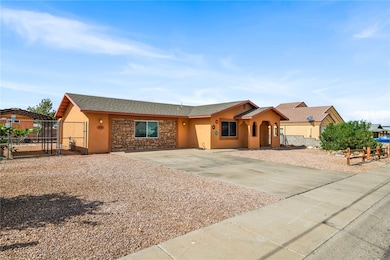 Single story home with stone siding, driveway, roof with shingles, stucco siding, and a gate