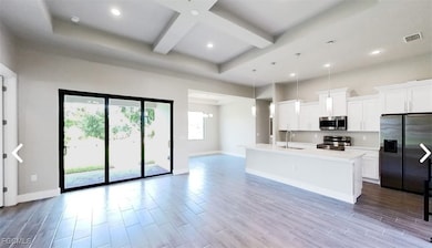 Kitchen with fridge with ice dispenser, hanging light fixtures, white cabinets, beamed ceiling, and a kitchen island with sink