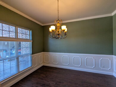 Unfurnished Dining room featuring wainscoting, crown molding, a decorative wall, dark wood-style flooring, and a chandelier