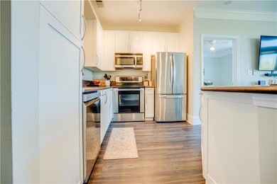 Kitchen with appliances with stainless steel finishes, white cabinetry, crown molding, and light wood-style floors