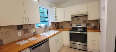 Kitchen featuring appliances with stainless steel finishes, open shelves, wood counters, under cabinet range hood, and lofted ceiling