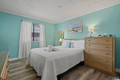Bedroom featuring wood finished floors, crown molding, baseboards, and a textured ceiling
