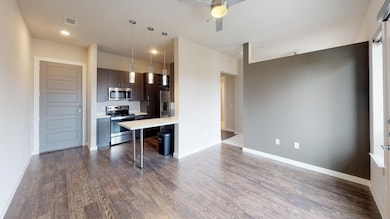 Kitchen featuring ceiling fan, a kitchen breakfast bar, dark hardwood / wood-style flooring, stainless steel appliances, and decorative light fixtures
