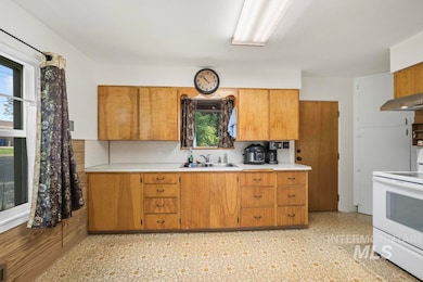 Kitchen featuring light countertops, white electric range oven, decorative backsplash, brown cabinets, and light floors