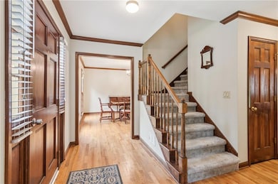 Foyer entrance with ornamental molding, light wood-style flooring, stairs, and baseboards