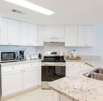 Kitchen featuring appliances with stainless steel finishes, light stone counters, white cabinets, under cabinet range hood, and light tile patterned flooring