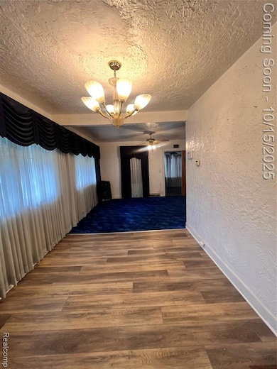 Spare room featuring a textured wall, a textured ceiling, dark wood finished floors, a chandelier, and ceiling fan