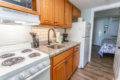 Kitchen featuring a sink, light wood-type flooring, white appliances, under cabinet range hood, and brown cabinets