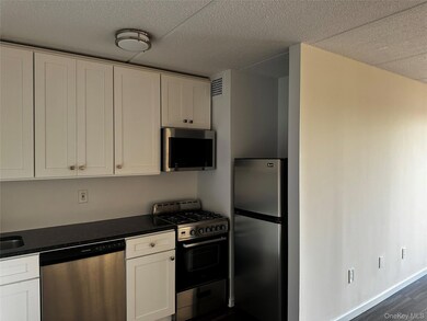 Kitchen with stainless steel appliances, white cabinets, dark wood-type flooring, a textured ceiling, and dark stone counters