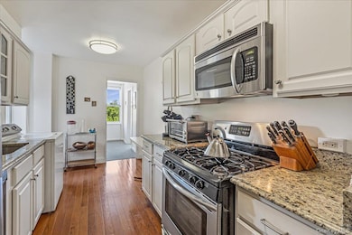 Kitchen featuring appliances with stainless steel finishes, washer / clothes dryer, light stone counters, dark wood-style flooring, and white cabinets