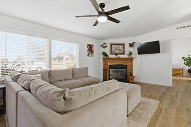 Living area featuring wood finished floors, a glass covered fireplace, and a ceiling fan