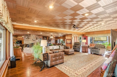 Living area with healthy amount of natural light, wood finished floors, ceiling fan, wood walls, and a large fireplace