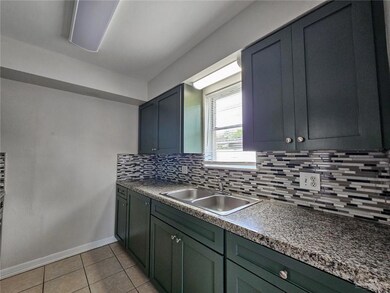 Kitchen featuring a sink, backsplash, light tile patterned floors, and baseboards