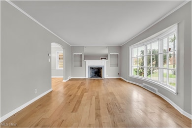 Unfurnished living room with arched walkways, a high end fireplace, crown molding, light wood-style floors, and radiator