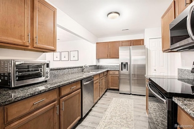 Kitchen with appliances with stainless steel finishes, dark stone counters, light wood-style flooring, and brown cabinetry