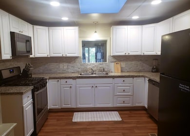 kitchen featuring appliances with stainless steel finishes, white cabinetry, dark wood-type flooring, a skylight, and pendant lighting