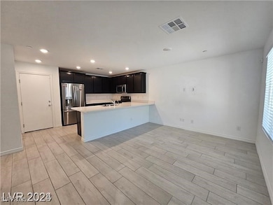 Kitchen featuring appliances with stainless steel finishes, a peninsula, wood finish floors, dark cabinetry, and recessed lighting