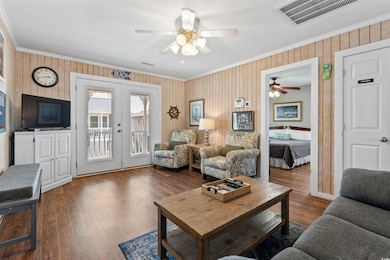 Living area with ornamental molding, french doors, a ceiling fan, wood finished floors, and wood walls