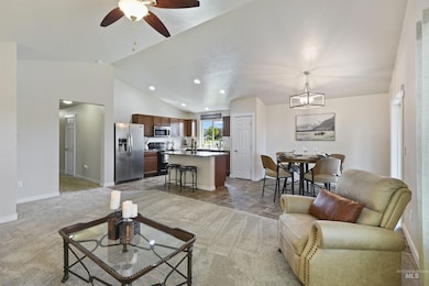 Living area featuring ceiling fan, vaulted ceiling, recessed lighting, light colored carpet, and a chandelier