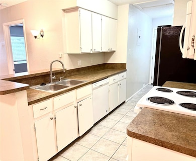 Kitchen featuring dark countertops, white cabinetry, white appliances, light tile patterned floors, and a peninsula