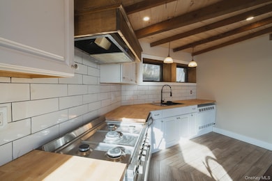Kitchen featuring wood counters, white cabinetry, decorative backsplash, stainless steel range oven, and ventilation hood