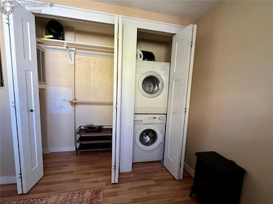 Laundry room featuring wood finished floors, stacked washer / dryer, and electric panel