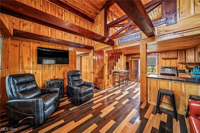 Living area featuring wood walls, stairway, dark wood-type flooring, and a wooden ceiling with exposed beams