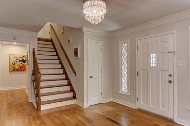 Foyer with ornamental molding, stairway, light wood-style flooring, a chandelier, and plenty of natural light