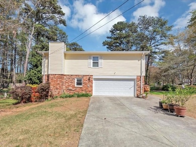 View of home's exterior with driveway, a chimney, brick siding, a garage, and a yard