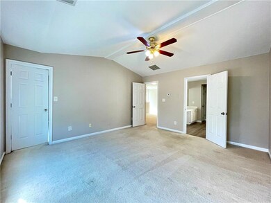 Unfurnished bedroom featuring lofted ceiling, light colored carpet, ensuite bath, and a ceiling fan