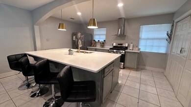 Kitchen with stainless steel range with gas stovetop, wall chimney exhaust hood, black fridge, light tile patterned floors, and arched walkways