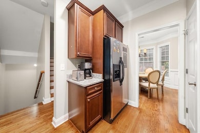 Kitchen featuring stainless steel fridge with ice dispenser, light wood-style flooring, crown molding, light stone countertops, and brown cabinetry
