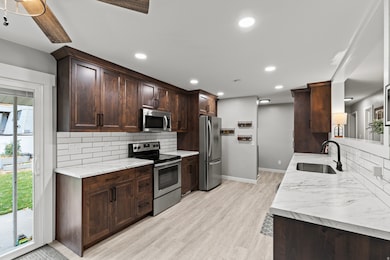 Kitchen with appliances with stainless steel finishes, backsplash, dark brown cabinets, light wood-type flooring, and recessed lighting