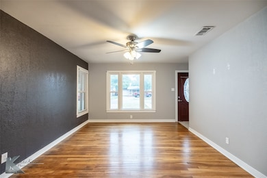 Spare room featuring light wood finished floors, a textured wall, and ceiling fan