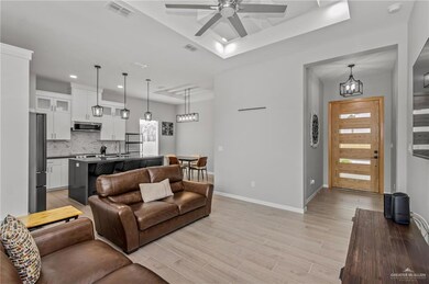 Living room with ceiling fan with notable chandelier, a tray ceiling, light hardwood / wood-style floors, and sink