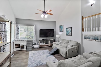 Living room with a ceiling fan, high vaulted ceiling, and wood finished floors