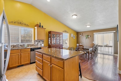 Kitchen with dark stone counters, tasteful backsplash, vaulted ceiling, a center island, and freestanding refrigerator