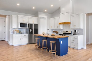 Kitchen with butcher block counters, tasteful backsplash, stainless steel appliances, a kitchen bar, and light wood finished floors