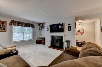 Living room featuring a fireplace, carpet, built in shelves, baseboards, and a textured ceiling