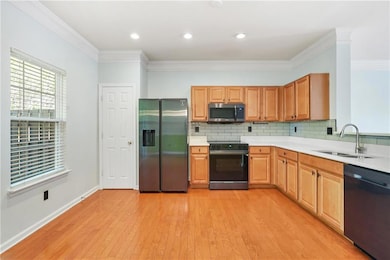 Kitchen with appliances with stainless steel finishes, a sink, light countertops, decorative backsplash, and ornamental molding