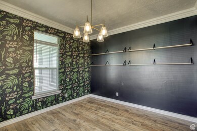 Unfurnished room featuring wood finished floors, wallpapered walls, ornamental molding, a chandelier, and a textured ceiling