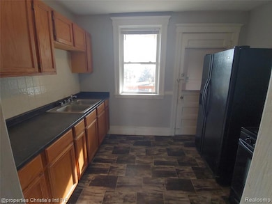 Kitchen featuring dark countertops, black appliances, brown cabinetry, and decorative backsplash