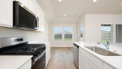 Kitchen featuring appliances with stainless steel finishes, white cabinets, recessed lighting, light wood-style floors, and light stone countertops