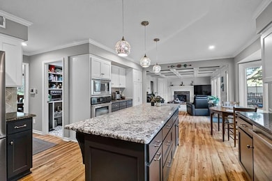 Kitchen featuring ornamental molding, coffered ceiling, light wood finished floors, dark stone counters, and a fireplace