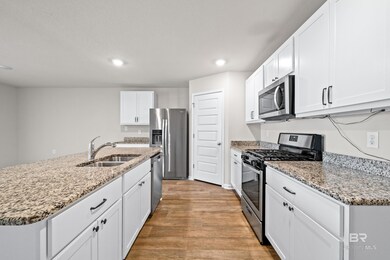 Kitchen with sink, light hardwood / wood-style flooring, white cabinetry, stainless steel appliances, and light stone countertops