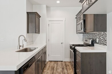 Kitchen with appliances with stainless steel finishes, light wood-style floors, dark brown cabinets, light stone countertops, and decorative backsplash