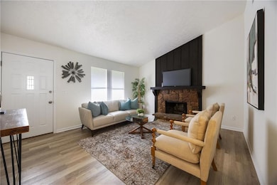 Living room with light wood-type flooring, a stone fireplace, a textured ceiling, and vaulted ceiling