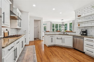 Kitchen with stainless steel appliances, wall chimney range hood, white cabinetry, backsplash, and recessed lighting